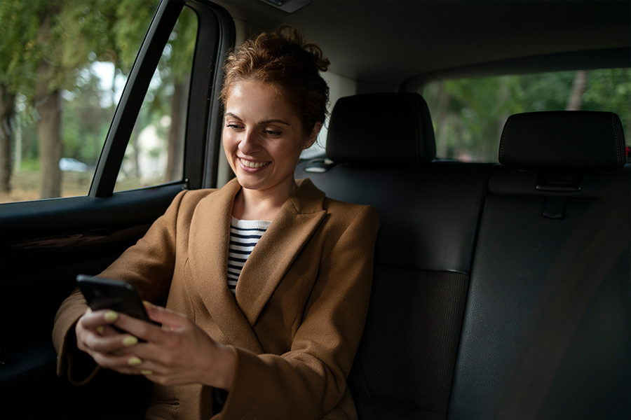 A woman in the backseat of a private taxi, relaxed and smiling on her way to her destination